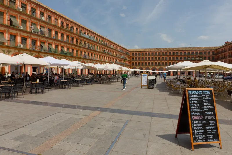 La plaza de la Corredera, rectangular y porticada, con sus fachadas rojizas, balcones y terrazas con sombrillas blancas.